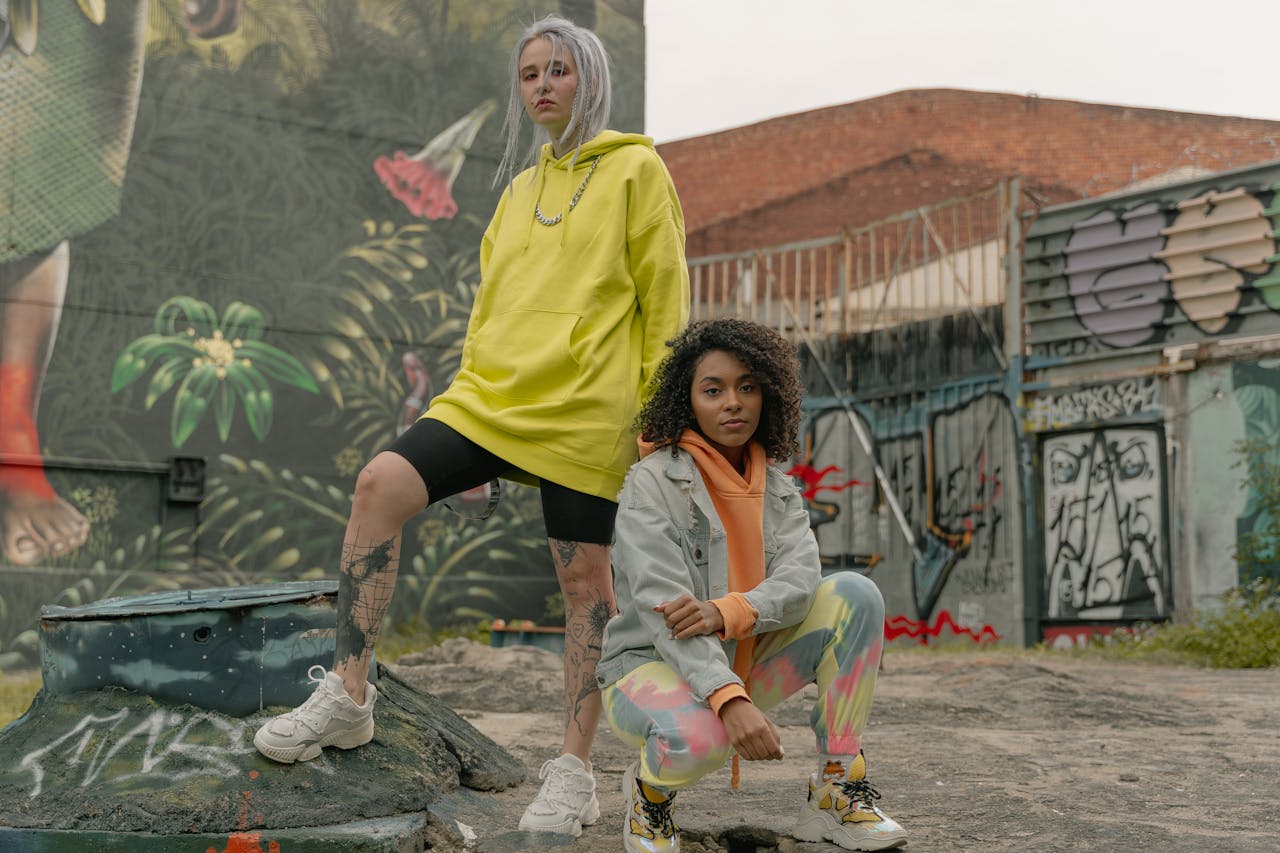 Two diverse women pose stylishly against a vibrant graffiti backdrop.