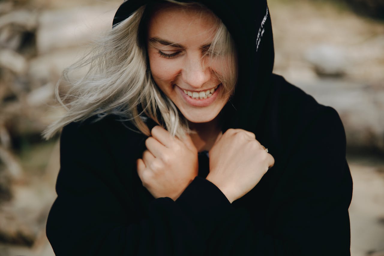 Close-up of a blonde woman smiling with crossed arms in a black hoodie.